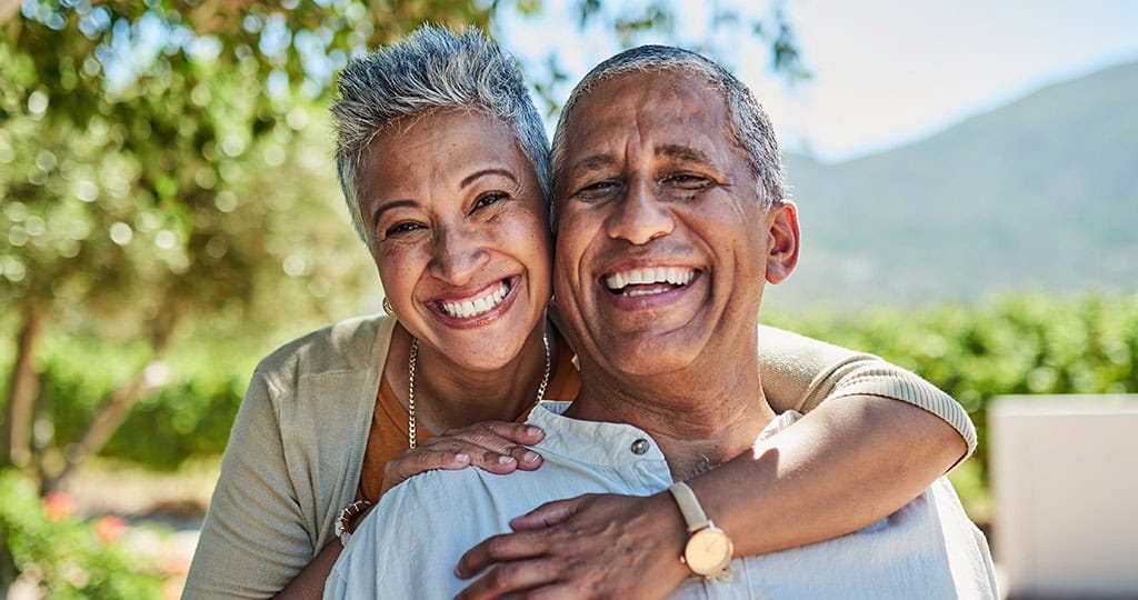 Smiling senior woman hugging husband while standing outside in summer