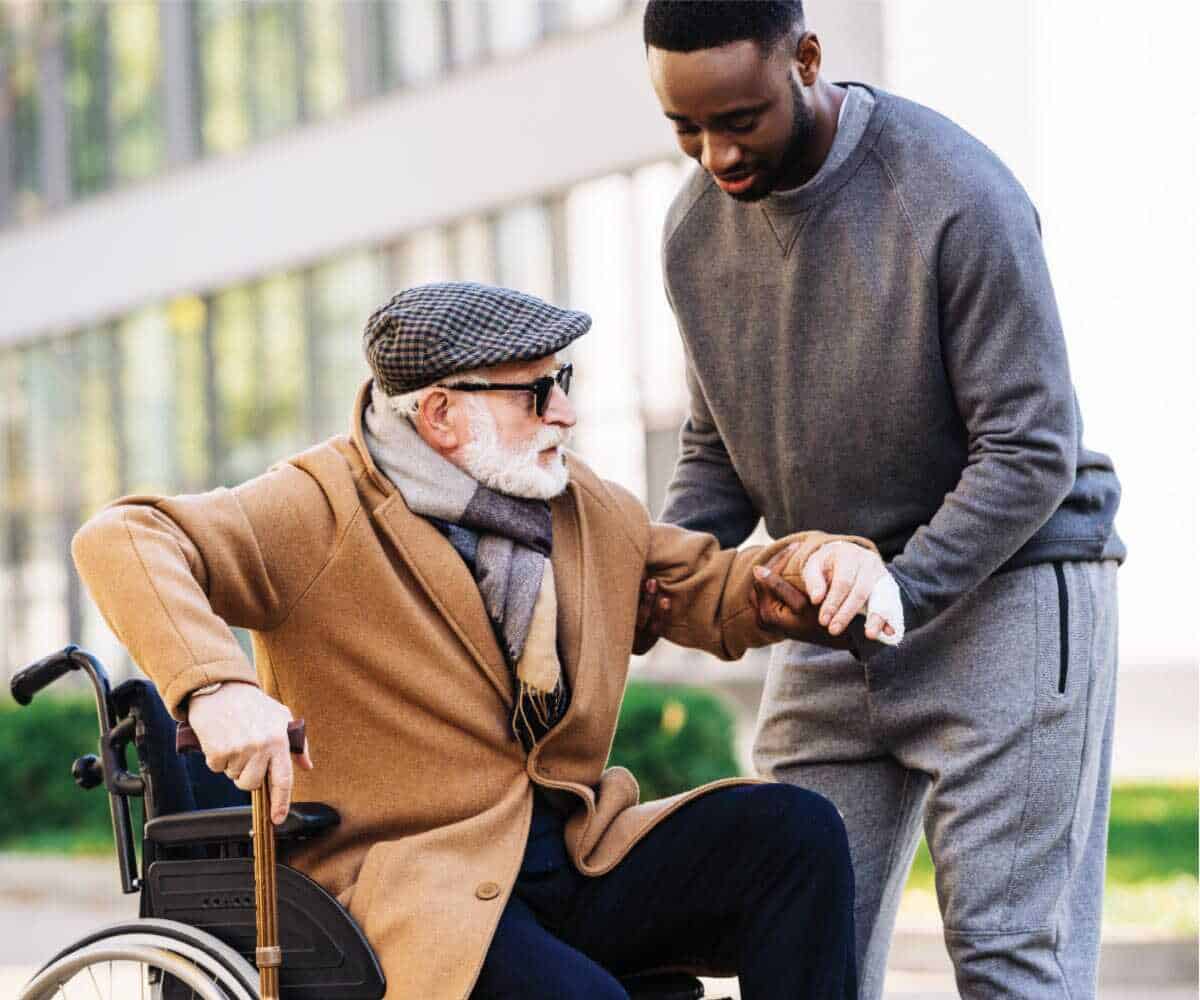 A man in a wheelchair is providing home CARE for another man in a wheelchair.