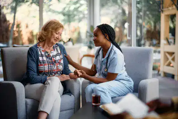 EMPOWERING FAMILIES WITH COMPREHENSIVE IN-HOME CARE 3 A NURSE REPRESENTING A HOME CARE AGENCY, HOLDS THE HAND OF AN ELDERLY WOMAN SEATED ON A CHAIR.